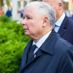Jarosław Kaczyński, lider partii, w czarnym płaszczu i z przypinką z polską flagą, podczas oficjalnych uroczystości.