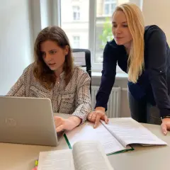 Dwie kobiety przy biurku analizują dokumenty i pracują na laptopie.
