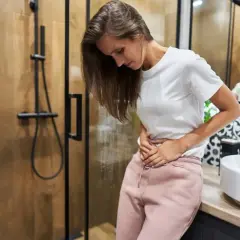 Kobieta w łazience trzyma się za brzuch, zaniepokojona. Czy to plamienie implantacyjne? Zdjęcia mogą pomóc w rozpoznaniu.