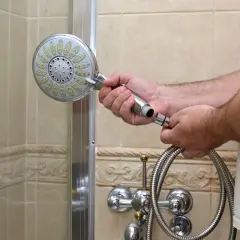 Mann wechselt die duschbrause. Er hält die alte Brause in der Hand und den Schlauch daneben.