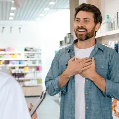 Mężczyzna z dłońmi na piersi rozmawia z farmaceutką, zastanawiając się, ile zarabia farmaceuta.