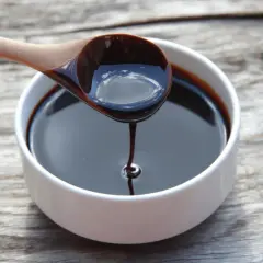 Gęsta, ciemna melasa spływa z drewnianej łyżki do białej miseczki. To właśnie melasa, słodki syrop z trzciny cukrowej.