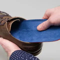 Braune Lederschuhe mit blauen Innenschuhen. Eine Hand hält die Einlage, die andere den Schuh.
