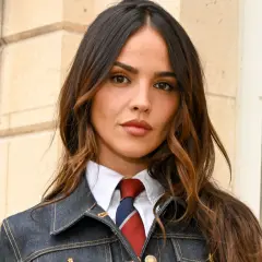 Mujer con cabello castaño y mechas woodlights, viste camisa blanca, corbata y chaqueta vaquera.