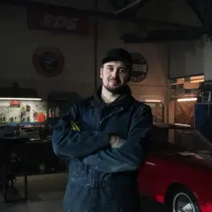 Mechanik w warsztacie z czerwonym autem. Co zrobić, gdy mechanik przetrzymuje auto? Zapytaj o fakturę i termin odbioru.