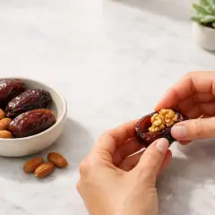 Mani che preparano datteri ripieni di noci. Un snack salutare con un basso indice glicemico, ideale per uno spuntino energetico.