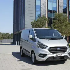 Furgoneta Ford Transit plateada cargando, con un edificio moderno al fondo. La presión de los neumáticos es clave para su eficiencia.