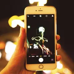 Dłoń trzyma smartfon, na ekranie którego widać interfejs aparatu. Można tu zobaczyć, jak zmienić aparat w telefonie, wybierając różne tryby fotografowania.