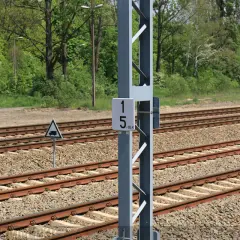 Słup z tabliczką 15-16,4, czyli hektometr kolejowy, obok torów kolejowych.