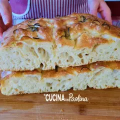 Focaccia alta e soffice, tagliata a metà, con rosmarino e sale grosso. La mollica alveolata promette un sapore delizioso.