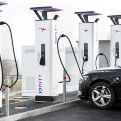 Une voiture électrique noire est branchée à une borne de recharge Ionity. Plusieurs bornes sont alignées, prêtes à alimenter les véhicules.