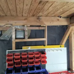 Pågår arbete för att isolera garage. Syns träbjälkar, isolering och förvaringssystem med fack.