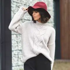 Kobieta w beżowym swetrze z warkoczami i bordowym kapeluszu.