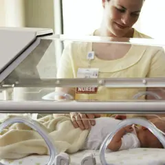 Pielęgniarka czule dotyka noworodka w inkubatorze. Dziecko urodziło się w 32. tygodniu ciąży, wymaga szczególnej opieki.