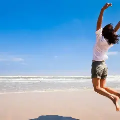 Szczęśliwa kobieta skacze na plaży, uosabiając, kim jest hedonista – czerpiąc radość z chwili.