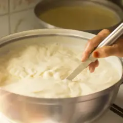 Mano che mescola un pentolone pieno di cremoso yogurt da bere fatto in casa, pronto per essere gustato.