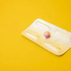 Tabletki dzień po bez recepty od kiedy? Jedna różowa tabletka w opakowaniu na żółtym tle.