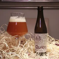 Szklanka bursztynowego piwa Quatro z pianką obok butelki. Czy to piwo, co to?