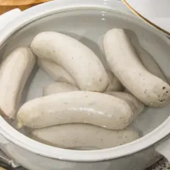 Biała kiełbasa w garnku, gotowa do parzenia. Delikatne, białe kiełbaski zanurzone w wodzie, czekają na idealny moment.