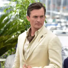 Hombre con un impecable corte de pelo old money, viste un traje de lino color crema y un pañuelo de seda.