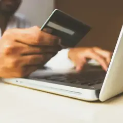 Mężczyzna z kartą płatniczą przed laptopem, szukający, gdzie zapłacić grzywnę z wyroku nakazowego.