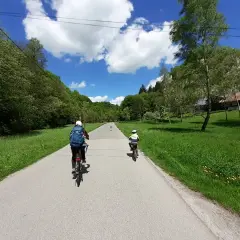 Dwie osoby na rowerach przemierzają malownicze **ojcowskie park narodowy trasy rowerowe**. Słoneczny dzień, zieleń i chmury na niebie.