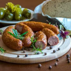 Wędzona kiełbasa na desce z ziołami i pieprzem. Idealna do chleba i ogórków. Zastanawiasz się, jaka sól do kiełbasy? Ta wygląda apetycznie!