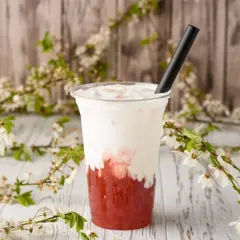 Jak zrobić bubble tea? Pyszny napój z truskawkowym syropem i mleczną pianką, ozdobiony kwitnącymi gałązkami.