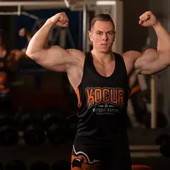 Mężczyzna w koszulce sportowej prezentuje umięśnione ramiona, inspirując do tego, jak zwiększyć masę mięśniową.