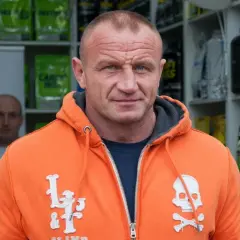 Mariusz Pudzianowski, znany jako Pudzian, w pomarańczowej bluzie z kapturem. Ile lat ma Pudzian? To pytanie nurtuje wielu fanów.