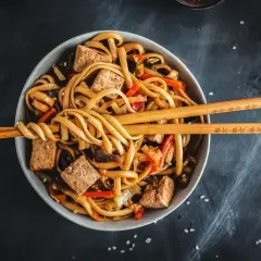 Miseczka pełna makaronu udon z tofu i warzywami, gotowa do jedzenia. Idealny makaron udon przepis na szybki obiad.