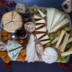 Un tagliere ricco di formaggi francesi, con pane, uva, albicocche secche e marmellata.