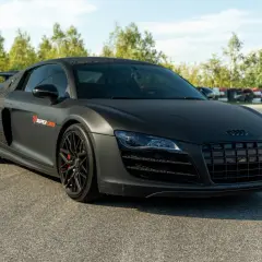 Matowy czarny Audi R8 V10 z czerwonymi zaciskami hamulcowymi na torze wyścigowym.