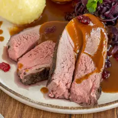 Saftiges Rehschulter Rezept: Rosa gebratenes Fleisch mit Sauce, Rotkohl und Klößen auf einem Teller.