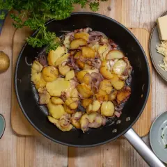 Bratkartoffeln aus rohen Kartoffeln, Zwiebeln und Speck in der Pfanne, dazu geriebener Käse und Petersilie.
