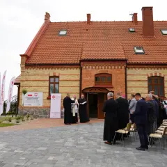 Uroczyste otwarcie centrum pomocowego Caritas im. Jana Pawła II. Grupa duchownych i wiernych zgromadzona przed budynkiem.