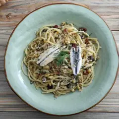 Assiette de pâtes au poisson italienne, garnie d'anchois, de pignons de pin et de raisins secs.