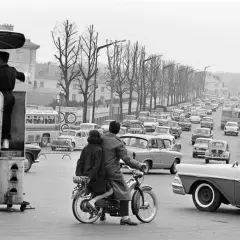 Un agent régule la circulation sur ce qui semble être la première autoroute de France, avec une file de voitures et un couple sur une mobylette.