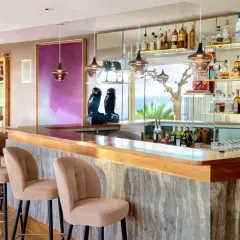 Un **majestic bar** avec des tabourets beiges, des étagères remplies de bouteilles et une vue sur la mer.