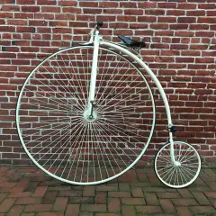 Ein Hochrad, ein Meilenstein in der Entwicklung Fahrrad, steht vor einer roten Ziegelwand.