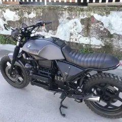 Moto BMW customizzata in stile cafe racer, con serbatoio grigio opaco, sella nera e borse moto laterali in pelle.