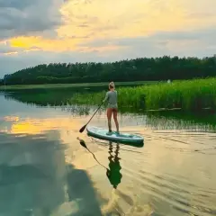 Kobieta na desce SUP, ciesząca się zachodem słońca nad jeziorem. Idealny czas na relaks, może nawet w okolicach Bożego Ciała.
