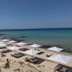 Traumhafter Karibik-Strand auf Chalkidiki mit weißen Sonnenschirmen und Liegen am türkisfarbenen Meer.