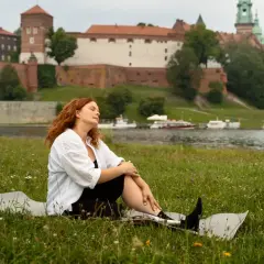 Kobieta z rudymi włosami odpoczywa na trawie z widokiem na Wawel. Idealne miejsce na jednodniowe wycieczki z Krakowa.