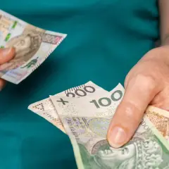 Dłonie trzymają polskie banknoty o nominałach 100, 200 i 500 zł.