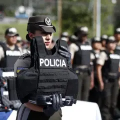 Agente de policía sostiene chaleco antibalas de material kevlar. Detrás, otros agentes uniformados.