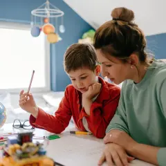 Mama z synem uczą się w domu. Czy edukacja domowa jest płatna? Na biurku globus, kredki i książki.