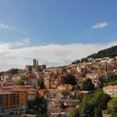 Widok na miasteczko na wzgórzu, z kolorowymi budynkami i zielenią, przypominający scenerię z festiwalu Cannes.