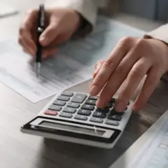 Osoba liczy na kalkulatorze, ile jest renty rehabilitacyjnej, wypełniając dokumenty.