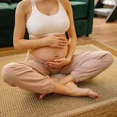 Donna incinta seduta a gambe incrociate sul tappeto, mani sull'addome. Si percepiscono i movimenti del feto a diverse altezze.